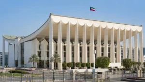 مبنى مجلس الأمة الكويتي بواجهته البيضاء المميزة وأعمدته المعمارية مع علم الكويت.